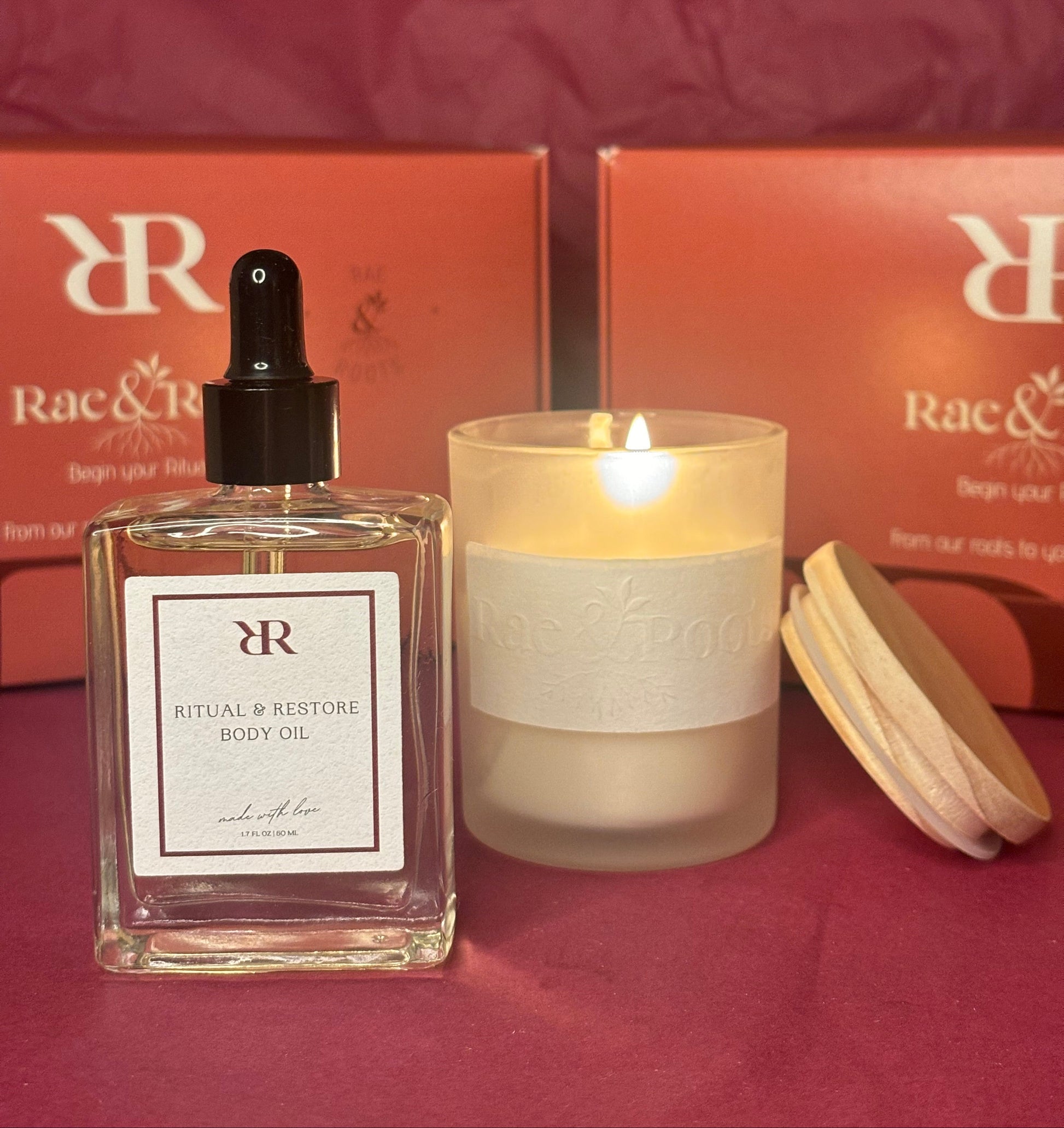 Rae & Roots body oil bottle and candle on a red surface with 'RR' branding.
